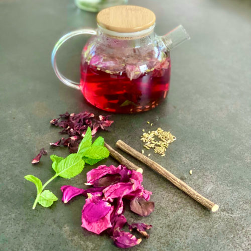 Red rose tea in a glass teapot with dried rose petals, hibiscus and fresh mint